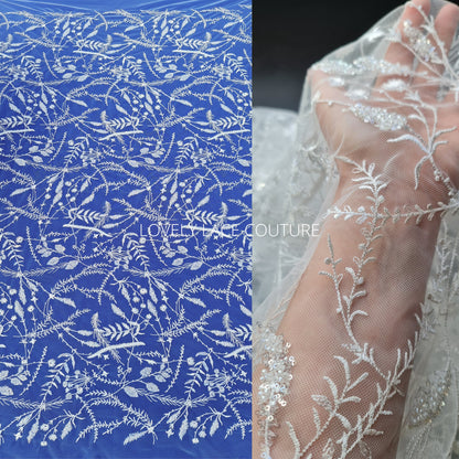 lace fabric with transparent buggle beads and sequins in white color on a blue background and shown on the hand